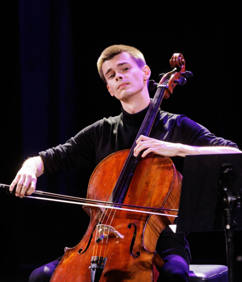 Cellist performing on a stage illuminated with purple light.