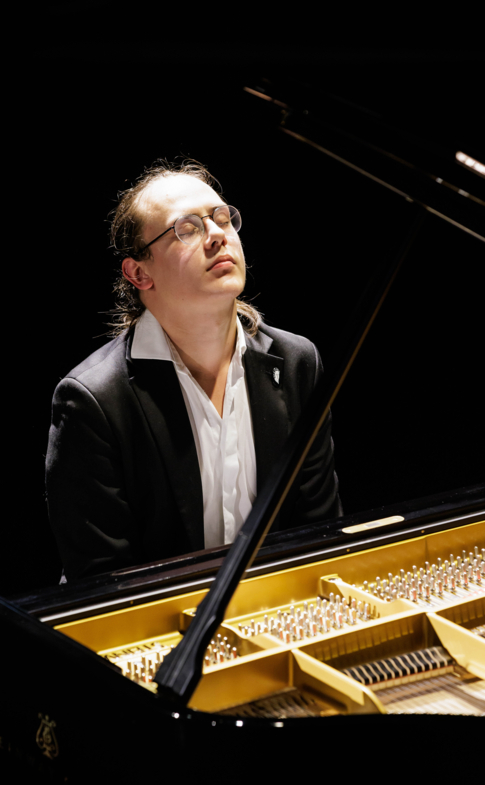 Close-up of a pianist with eyes closed while performing at a concert grand piano.