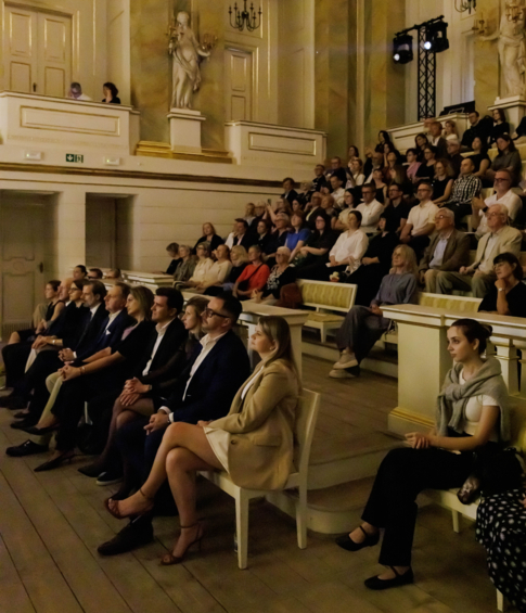 Audience attending a piano recital in an elegant historic concert hall.