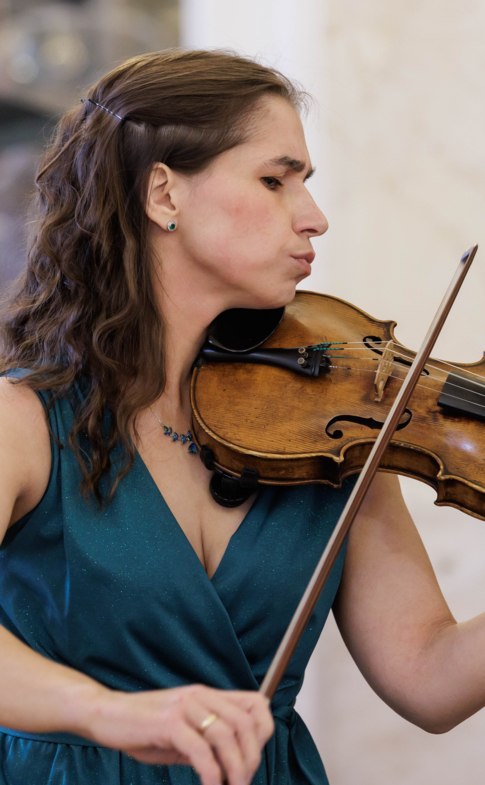 A violinist in a teal dress performs during a concert in an elegant interior.