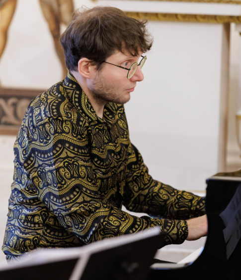 A pianist wearing glasses and a patterned shirt performs at a grand piano during a chamber music concert.
