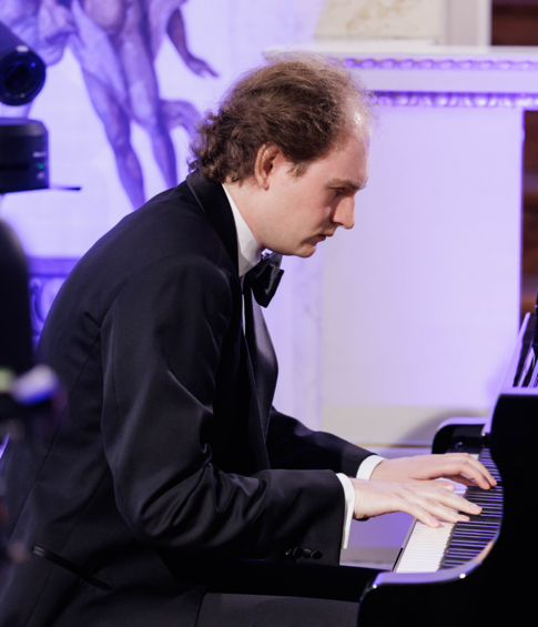 A pianist in a black tuxedo performs on a Shigeru Kawai grand piano during a recital.