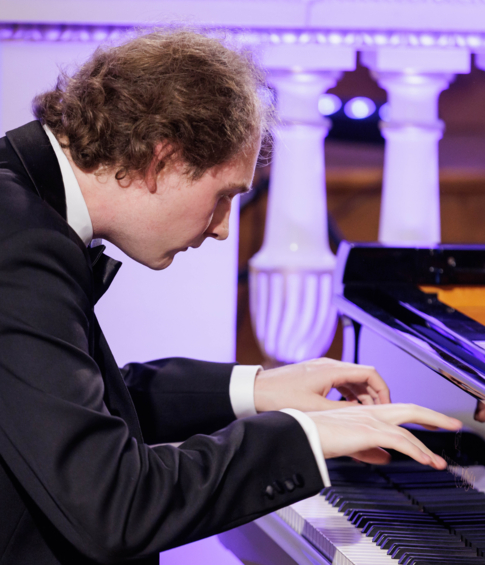 A pianist leans over the grand piano keyboard during an intense moment of his recital.