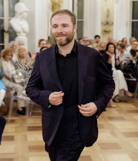 Uśmiechnięty pianista przechodzi obok publiczności, która oklaskuje go po występie.